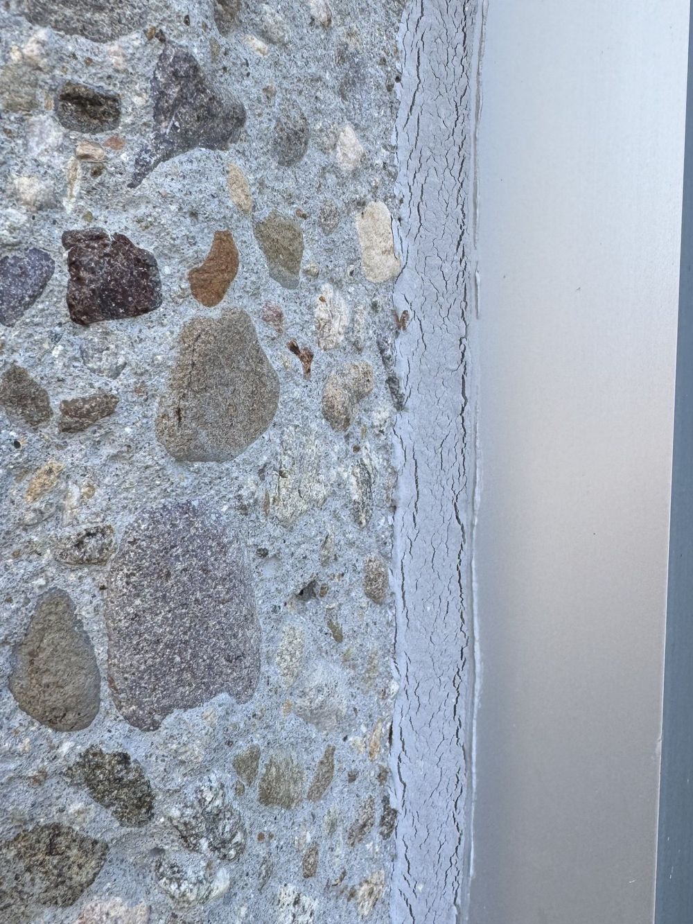 Failed window perimeter sealant at a precast concrete panel: the surface is crazed with cracks and the bead is releasing from the aluminum frame